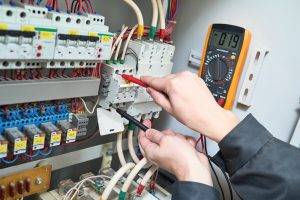 Hände mit Messgerät an einem geöffneten elektrischen Verteiler